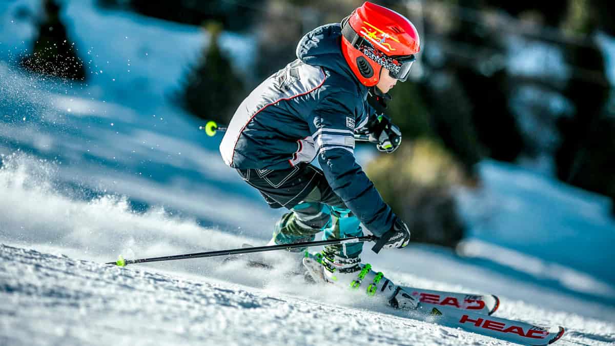Vibrant skier in winter gear racing down snow-covered mountain slopes during daytime.