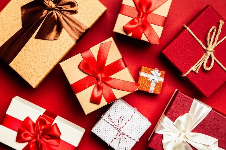 The best gifts for travelers this Christmas; gift boxes with red and gold wrapping, satin ribbons, and festive bows.