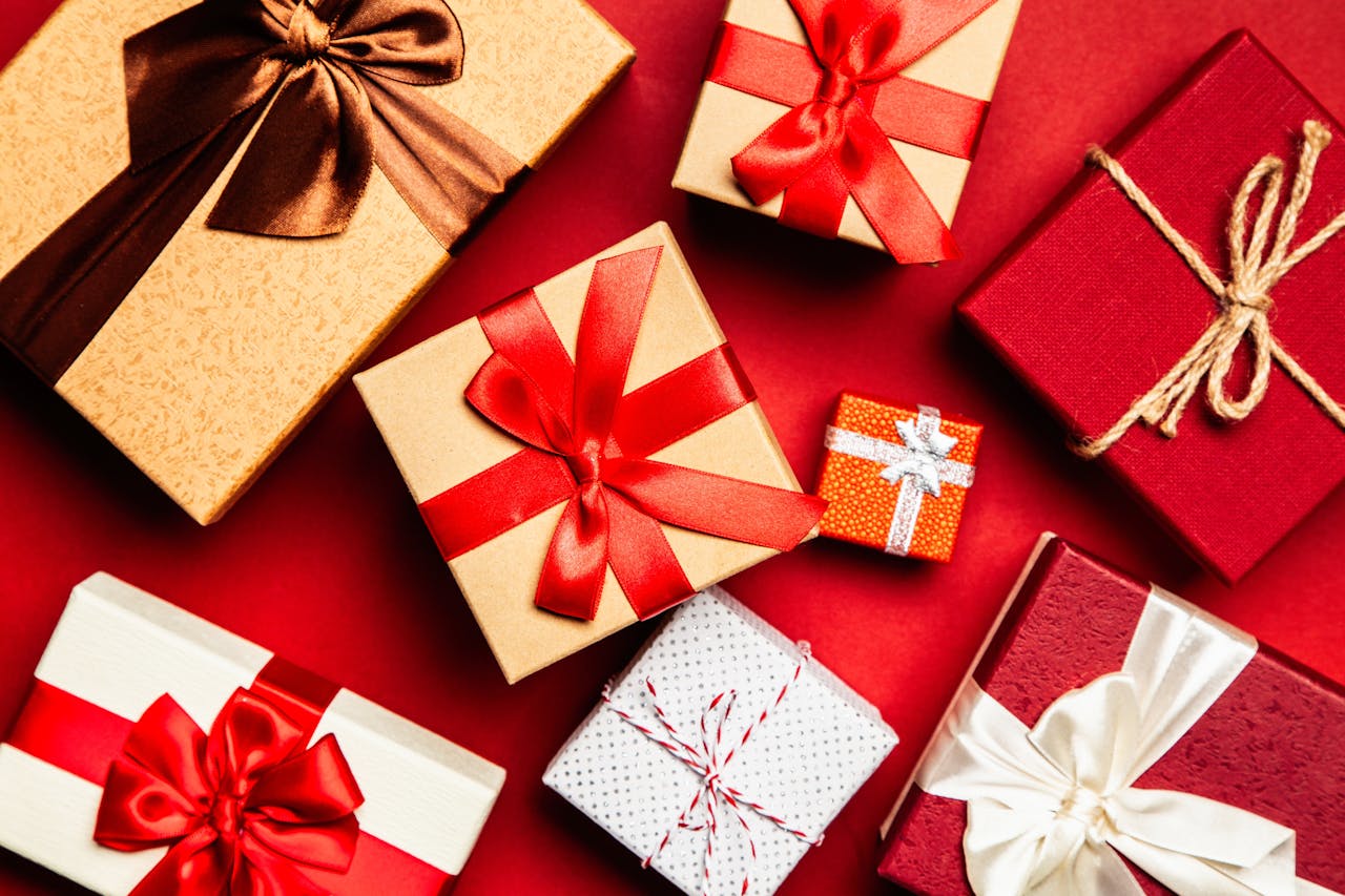 The best gifts for travelers this Christmas; gift boxes with red and gold wrapping, satin ribbons, and festive bows.