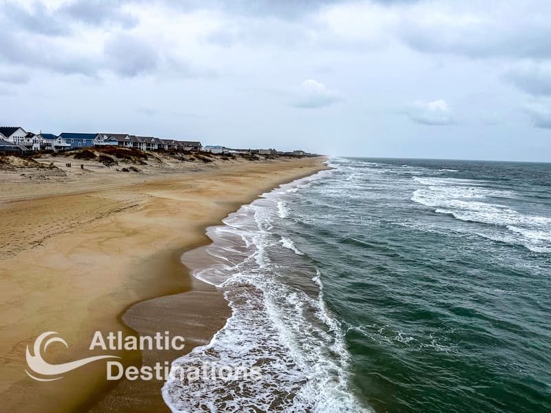 Beachfront view of Atlantic Ocean with sandy shore and coastal homes.