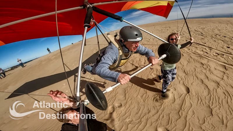 Paragliding adventure on a sandy beach with a man preparing to take off with a young boy, under a colorful parachute, capturing a fun outdoor activity.