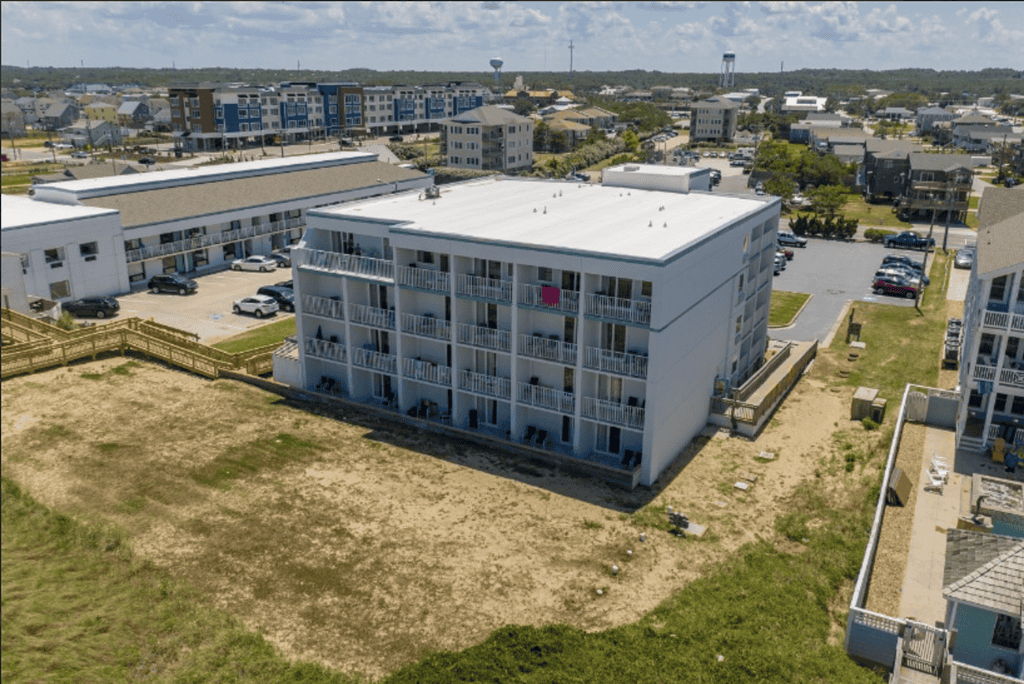 Aerial view of a modern, multi-story apartment building in Atlantic Destinations with surrounding residential and commercial areas under a clear sky.