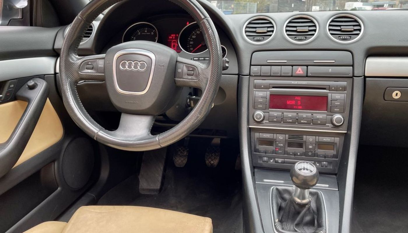 Innenraum eines Audi Fahrzeugs mit Schaltgetriebe, Mittelkonsole mit Audionavihilfe, Tacho und Lenkrad.