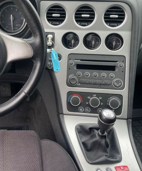 Hauptbild: Innenraum eines Autos mit Radio- und KlimakontROLLEN, Manuelle Schalttafel, Fahrzeuginstrumente sichtbar.