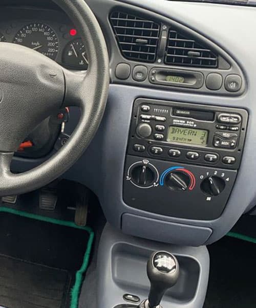 Altes Autoradio im Fahrzeugdashboard, mit Kassettenspieler und manuellen Klimareglern.