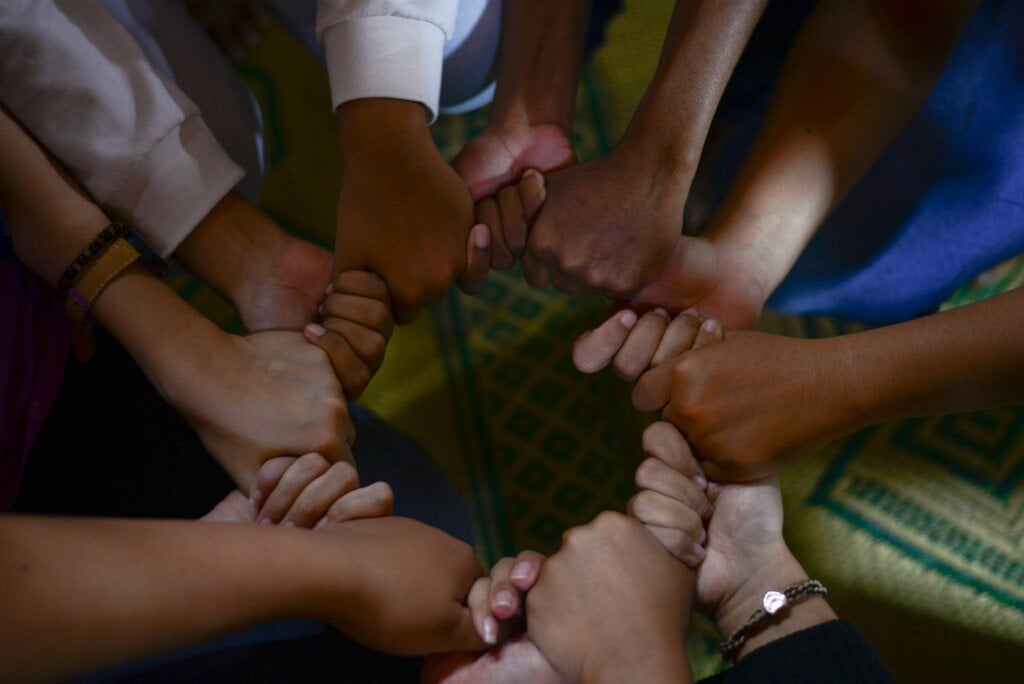 Mani di diverse persone che si tengono per mano formando un cerchio: simbolo dell'unità, della connessione e del legame umano che il dono crea.