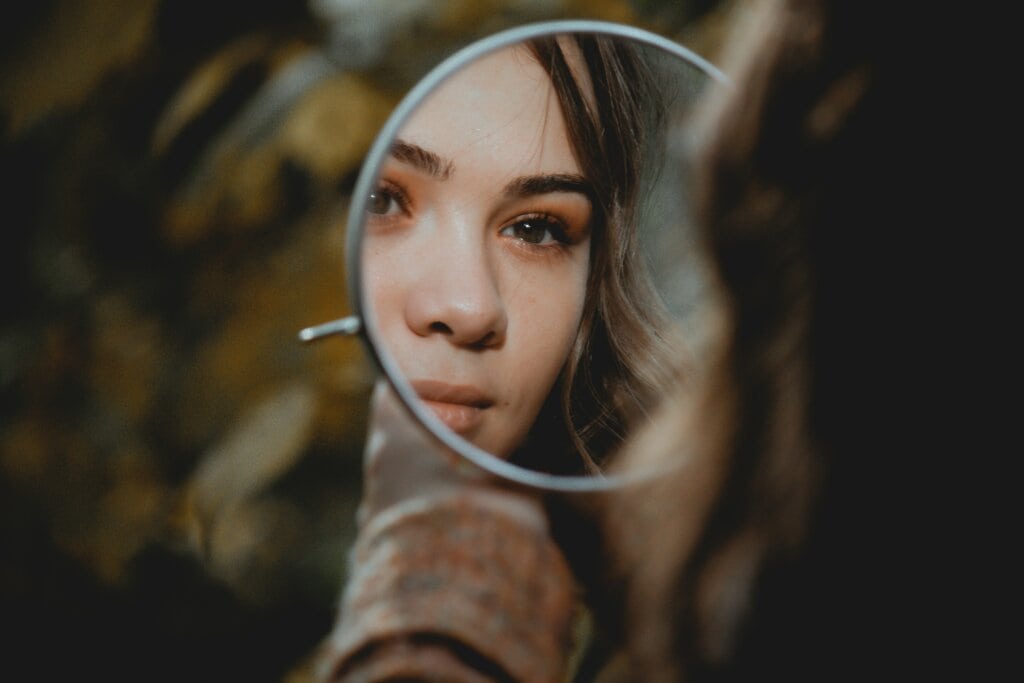 Giovane donna che si guarda in uno specchio rotondo. Immagine evocativa del ritrovare la propria identità (riferimento alla donazione di capelli per parrucche solidali oncologiche)