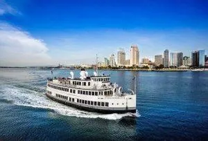A white passenger ferry cruising on a river near a city skyline under a clear blue sky.