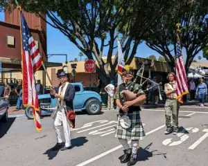 People in costume parade with flags and bagpipes.