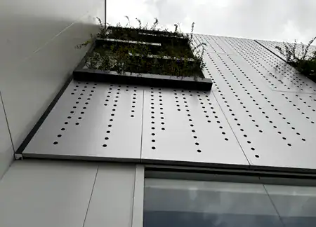 Fachada moderna con paneles perforados y vegetación
