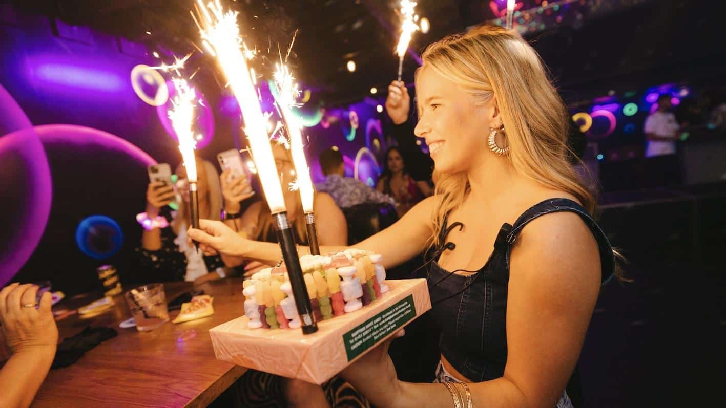 a girl carrying a VIP sweet cake to a table celebrating their birthday