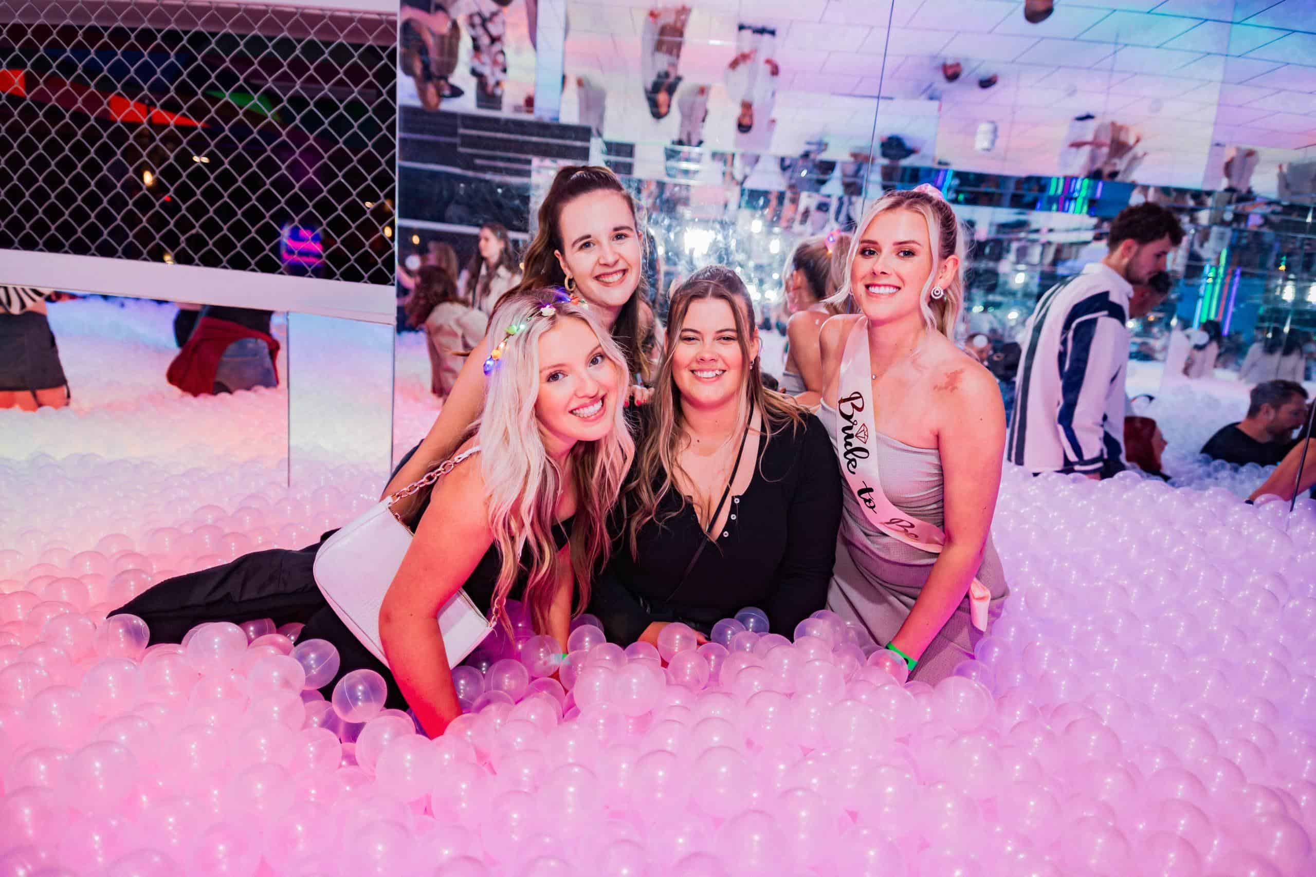 Colourful group of friends enjoying drinks and pizza at Ballie Ballerson, a famous London ball pit bar.
