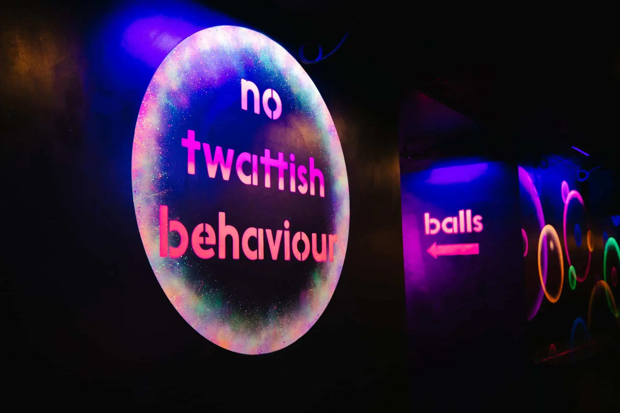 Glow-in-the-dark sign reading "no twattish behaviour" at Ballie Ballerson, London.