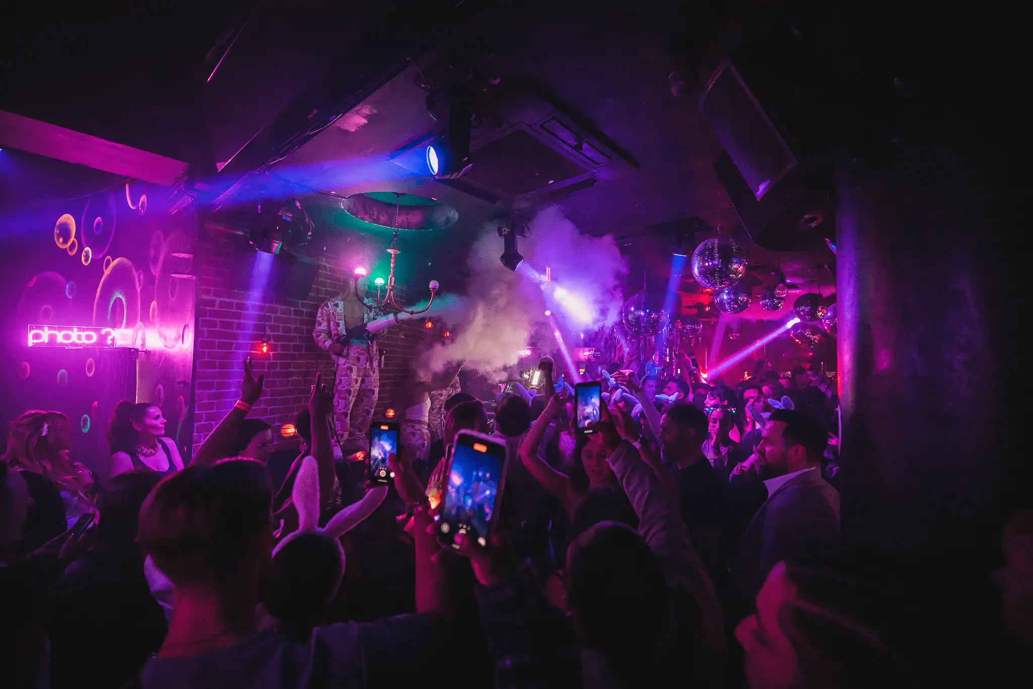 Vibrant nightclub scene with colourful lights, dancing crowd, and DJ performing at Ballie Ballerson.