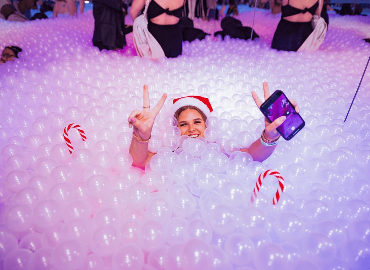 Vibrant ball pit with party guests, colourful lighting, fun atmosphere at Ballie Ballerson.