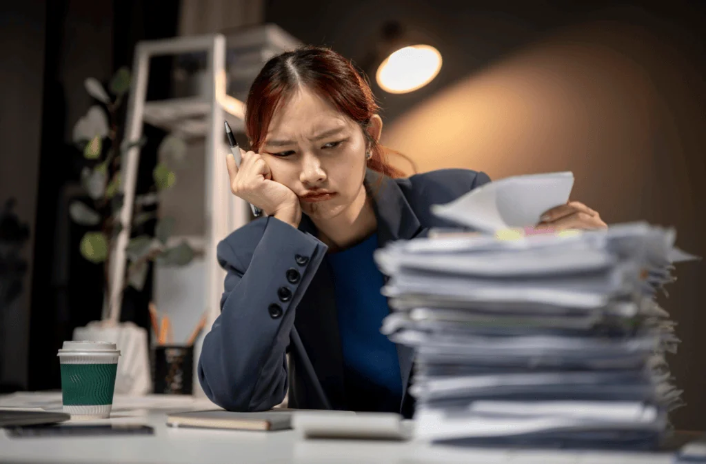 Frustrated woman overwhelmed with paperwork at her desk in an office setting.