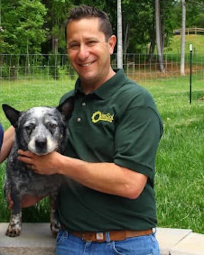 Man smiling with dog in a garden.