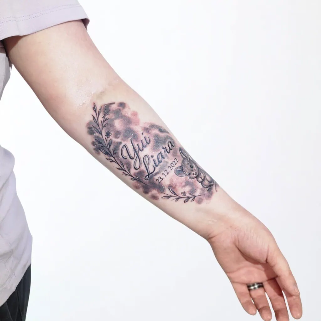 Familien Tattoo mit Namen «Yui Liara» und Datum 23.12.2021 – Maus und florale Elemente in sanften Farben, gestochen in Widnau.