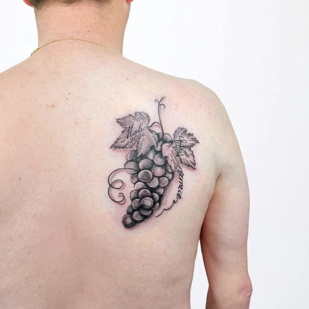 Trauben-Tattoo mit Blättern und Namen – symbolisches Enkel Tattoo auf dem Rücken, gestochen in Widnau.