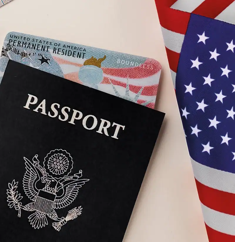 Green Card dos Estados Unidos parcialmente visível atrás de um passaporte americano e uma bandeira dos EUA, representando vistos de imigração para brasileiros que desejam morar legalmente nos Estados Unidos.