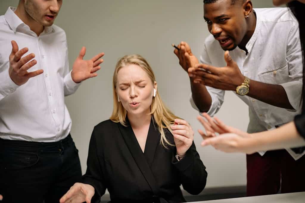 A Woman in Black Suit Sitting at the Table with three people talking to her and she is overwhelmed with being a neurodivergent at work.