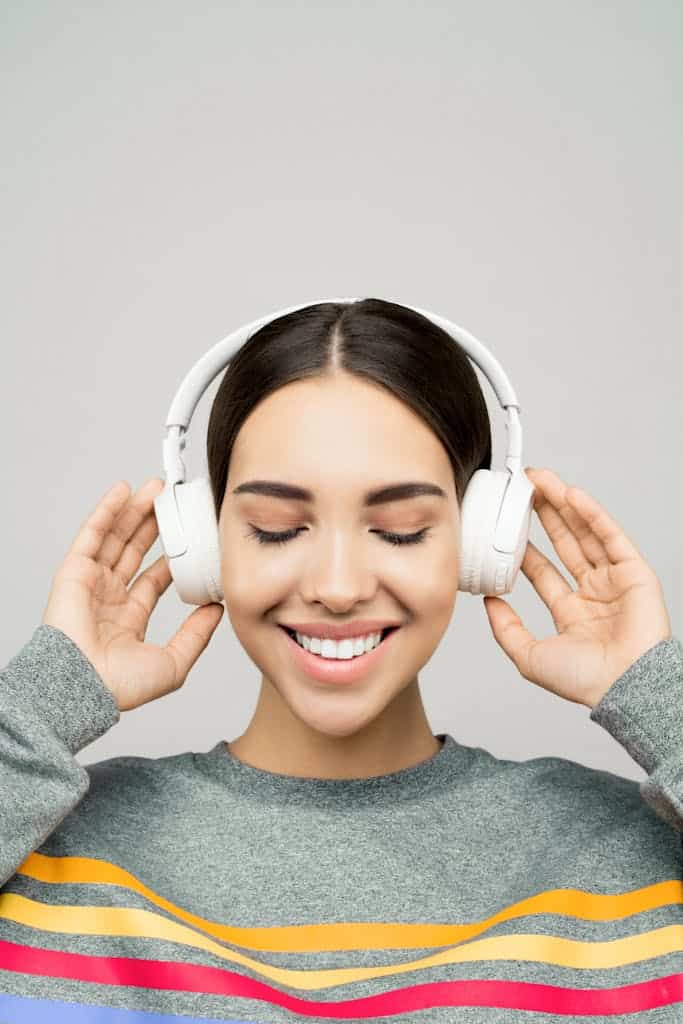 Woman in Gray Sweater Wearing White Headphones listening to music. 