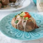 Single stuffed sweet potato on a blue plate, before cutting it apart to eat.