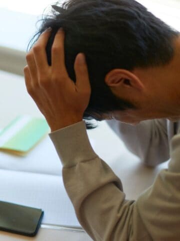 Man with hands placed on head, as in frustration, looking down at a work project.
