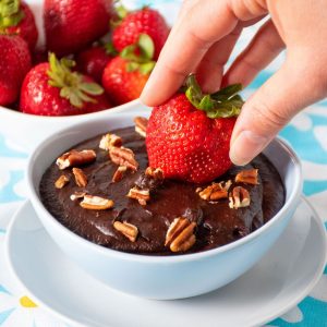 Strawberry being dipped into a bowl of brownie batter dip.