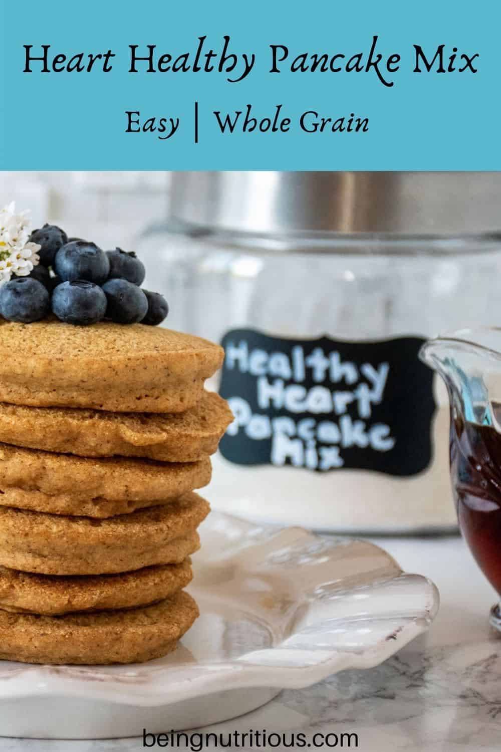 Stack of 6 whole wheat pancakes, with a pile of fresh blueberries on top. Glass jar that reads 'healthy heart pancake mix' is visible in the background.