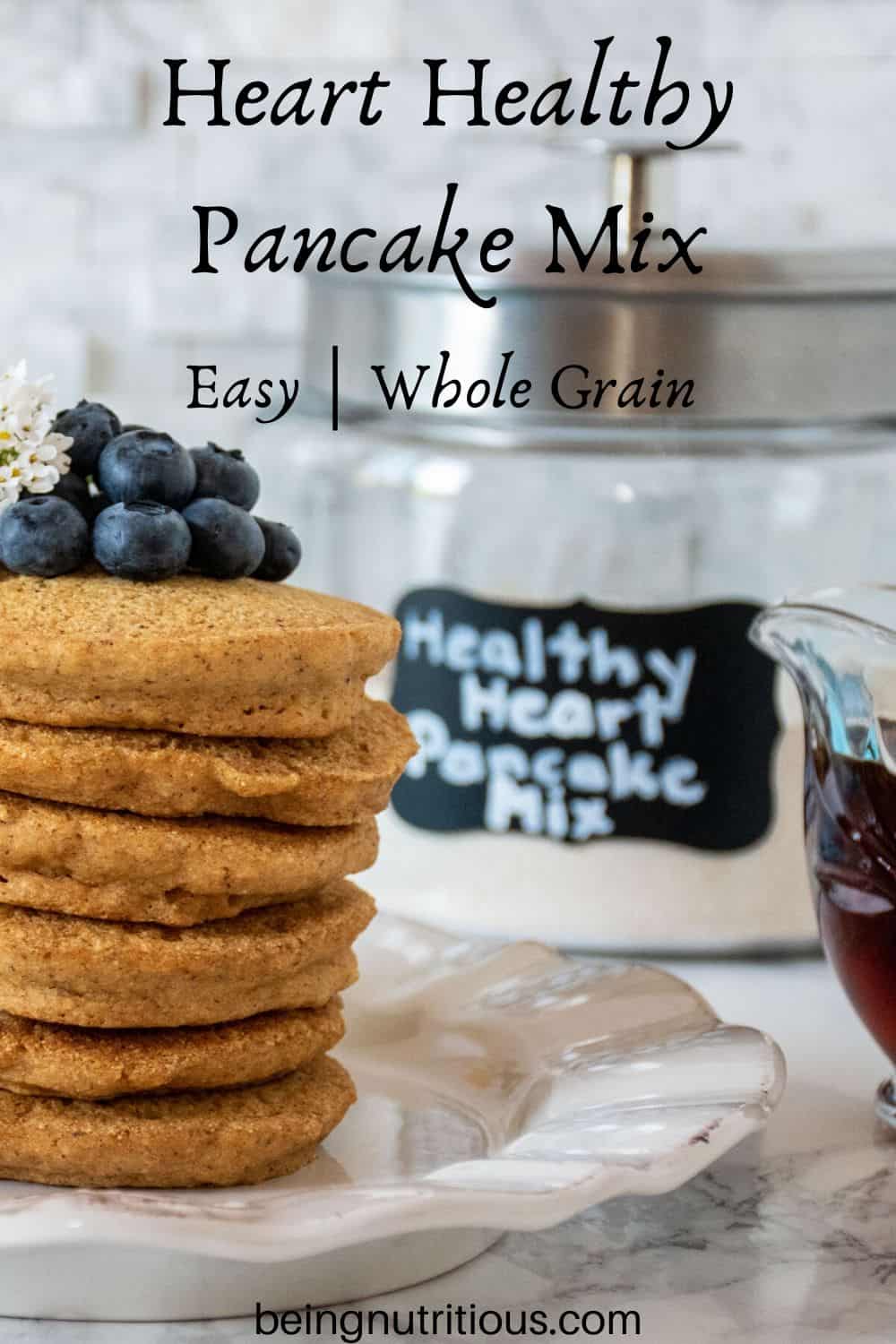 Stack of 6 whole wheat pancakes, with a pile of fresh blueberries on top. Glass jar that reads 'healthy heart pancake mix' is visible in the background.