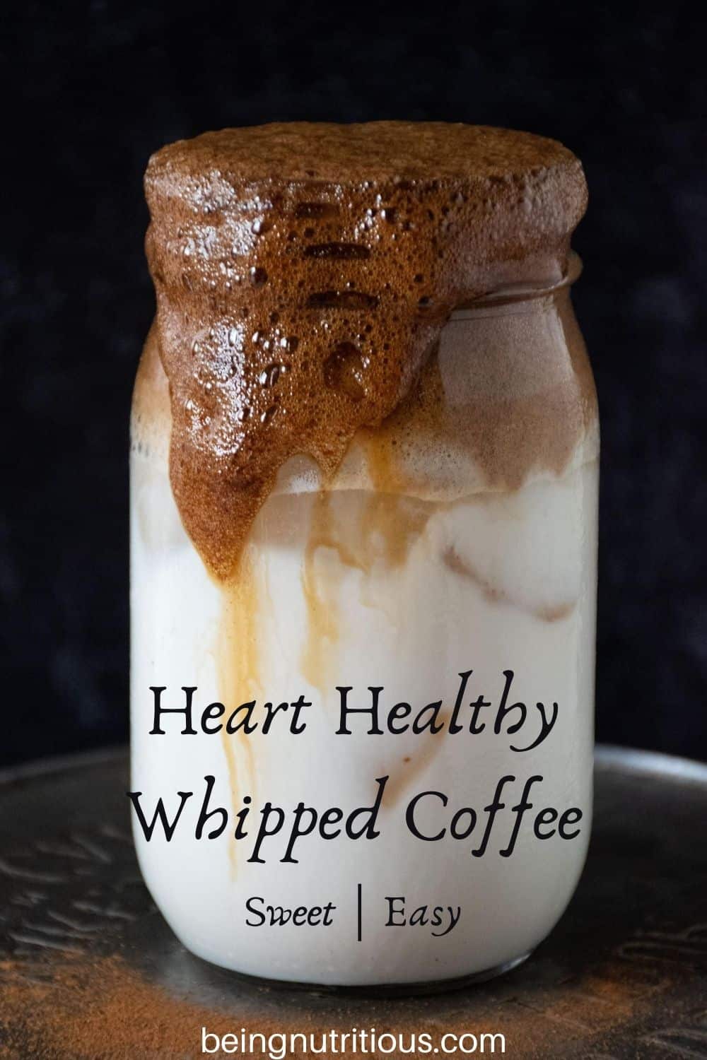 Whipped coffee over iced almond milk in a Mason jar with streams of coffee running down the side of the jar. Text overlay: &quote;Heart Healthy Whipped Coffee, sweet; easy"