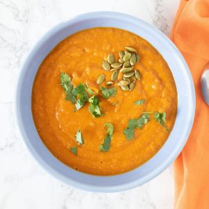 Overhead shot of pumpkin soup in a blue bowl, garnished with cilantro and pepitas.