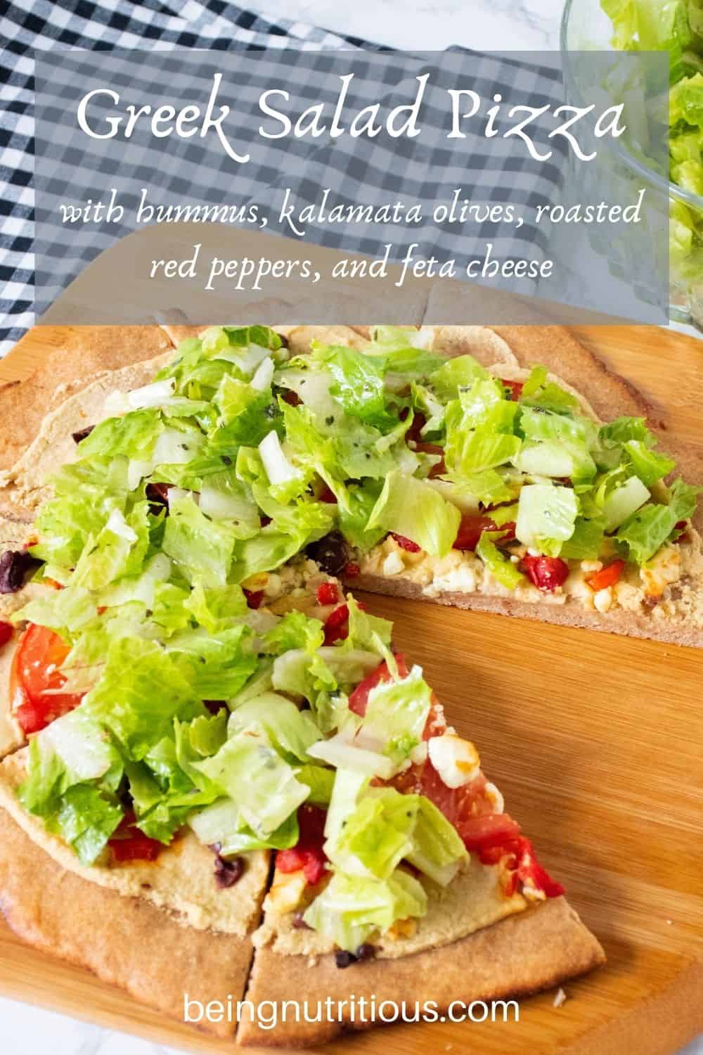 Pizza on a peel, with whole wheat crust, topped with salad. Text overlay: Greek Salad Pizza with hummus, kalamata olives, roasted red peppers, and feta cheese.
