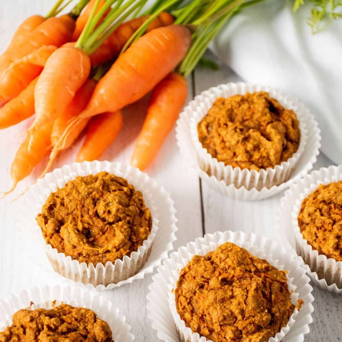 5 muffins on a table with fresh carrots.