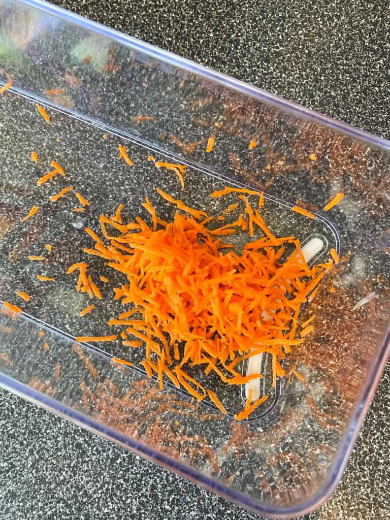 Carrots finely shredded in a clear plastic bin.