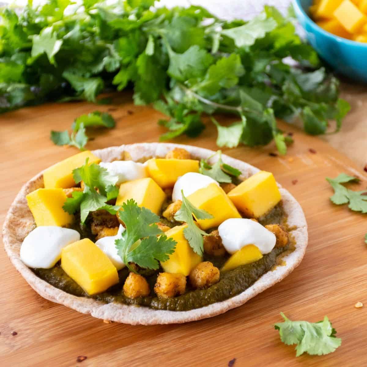 pizza with spinach sauce, chickpeas, and mangoes on a mini pita.