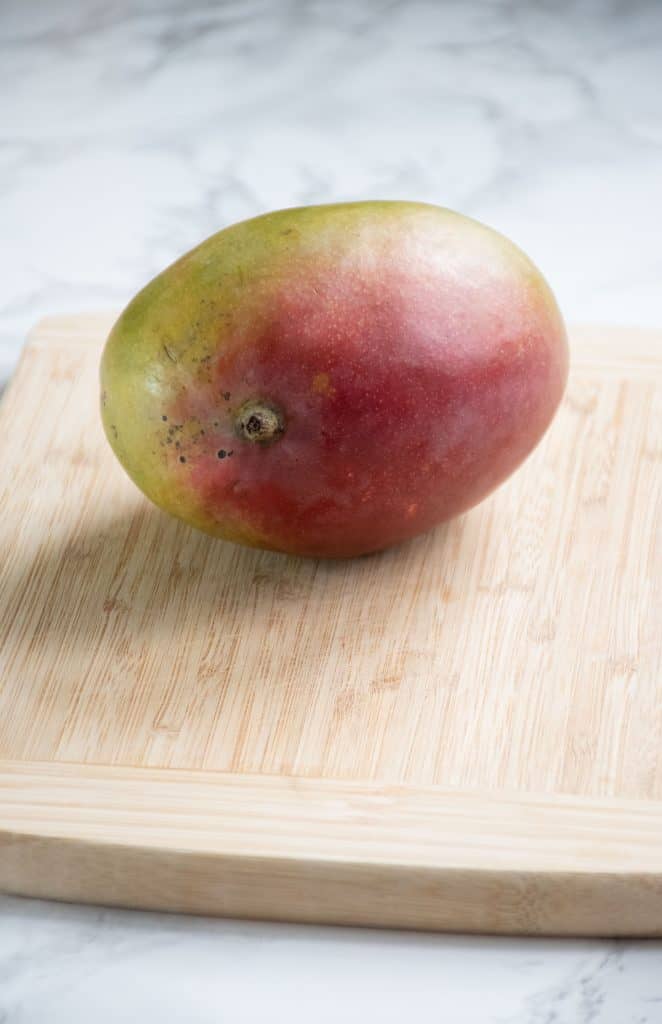 Whole mango on cutting board