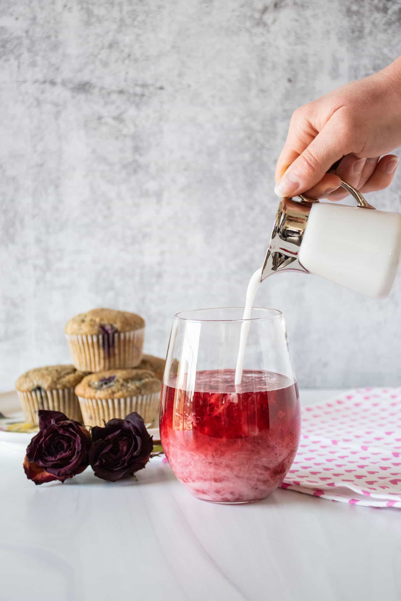 Glass of red, hibiscus tea, with coconut milk being poured in.