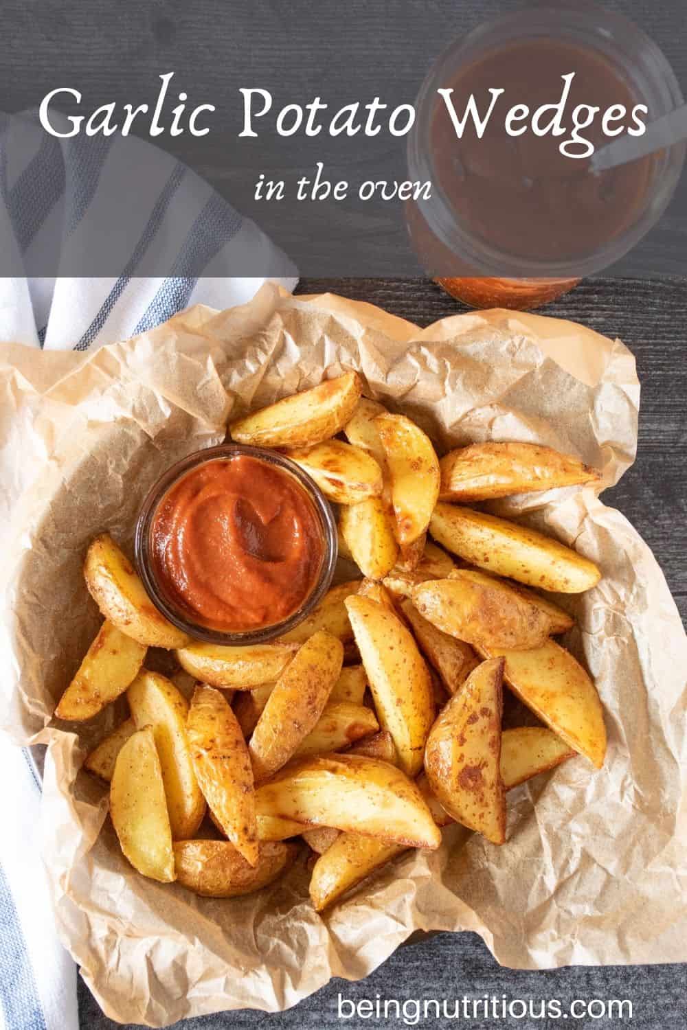 Basket of potato wedges with a small bowl of ketchup. Text overlay: Garlic Potato Wedges in the Oven.