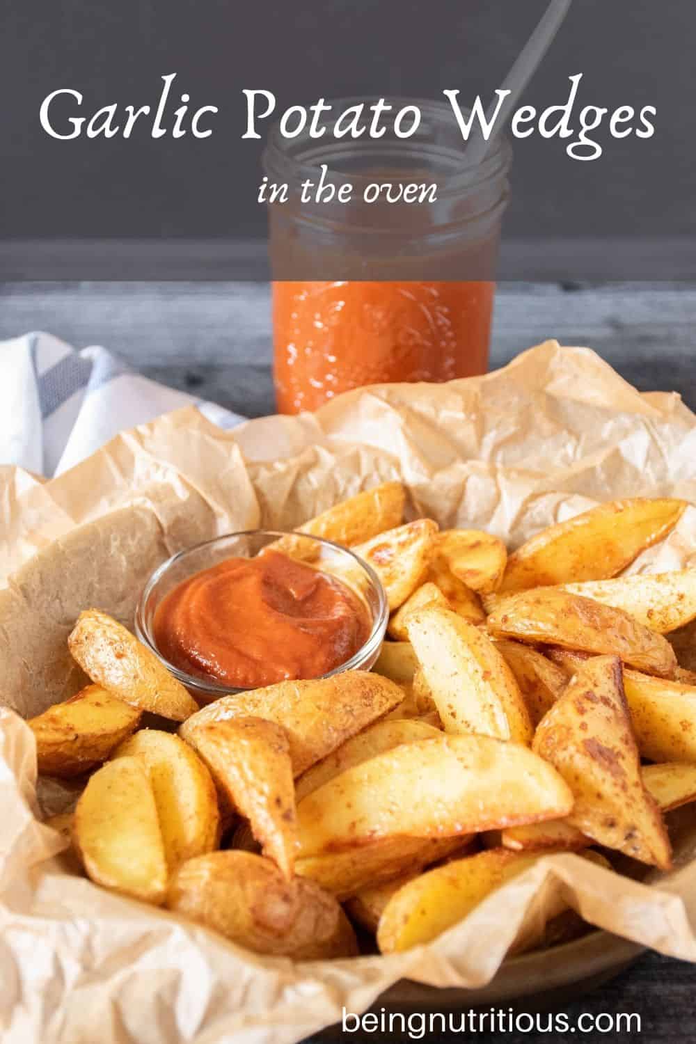 Basket of potato wedges with a small bowl of ketchup. Text overlay: Garlic Potato Wedges in the Oven.