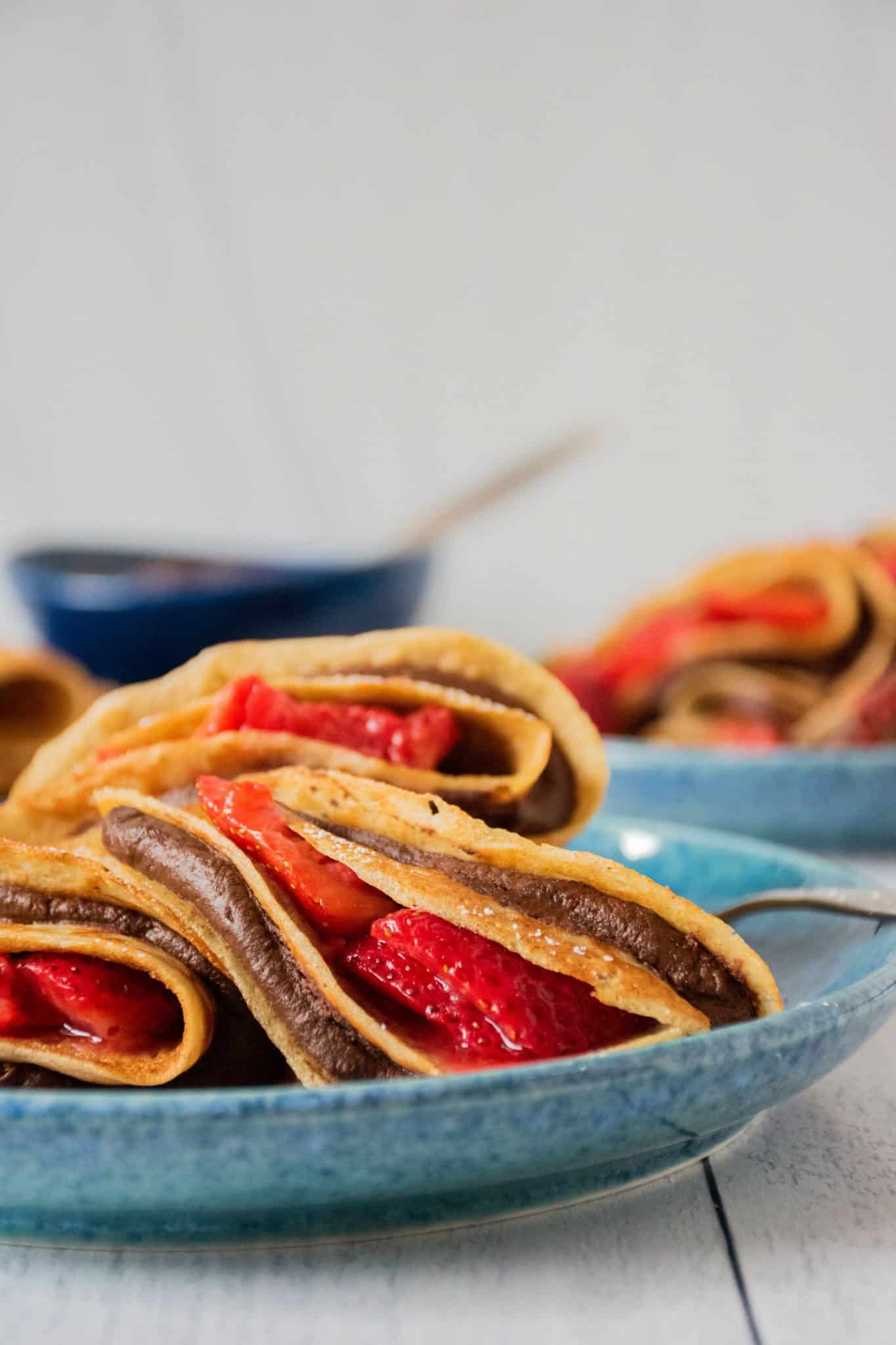 Plate of 3 crepes stuffed with chocolate dip and strawberries.