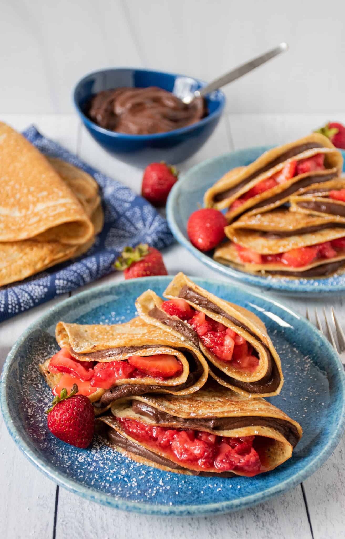 Plate of 3 crepes stuffed with chocolate dip and strawberries.