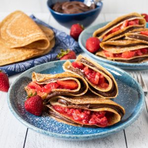 Plate of 3 crepes stuffed with chocolate dip and strawberries.