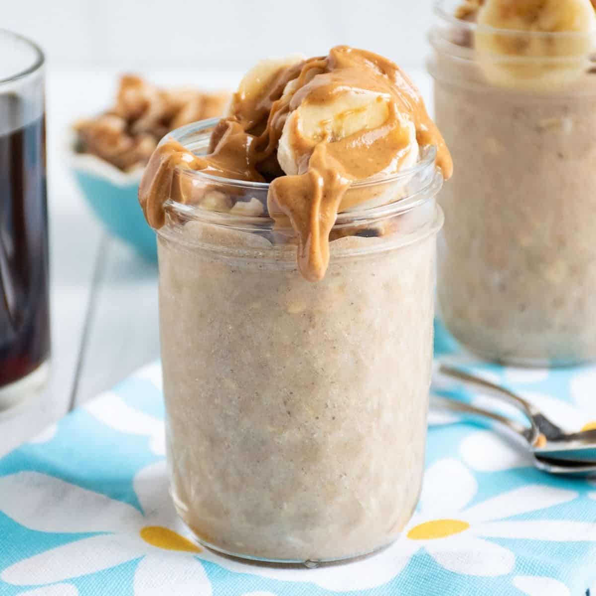 Small mason jar of oatmeal with walnuts and banana slices on top, with a drizzle of peanut butter