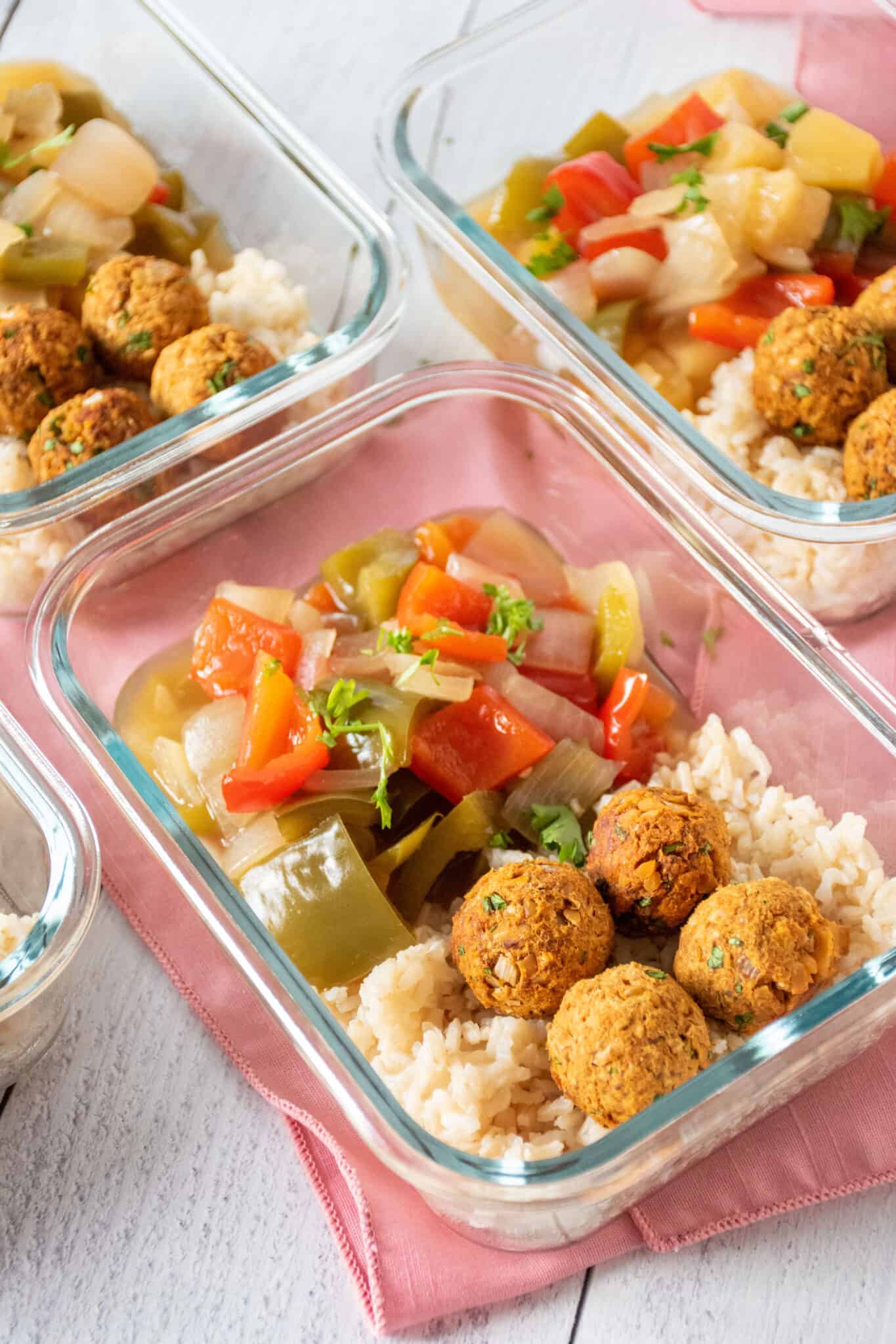 Glass meal prep containers, filled with rice, vegetarian chickpea meatballs, and onions and peppers.