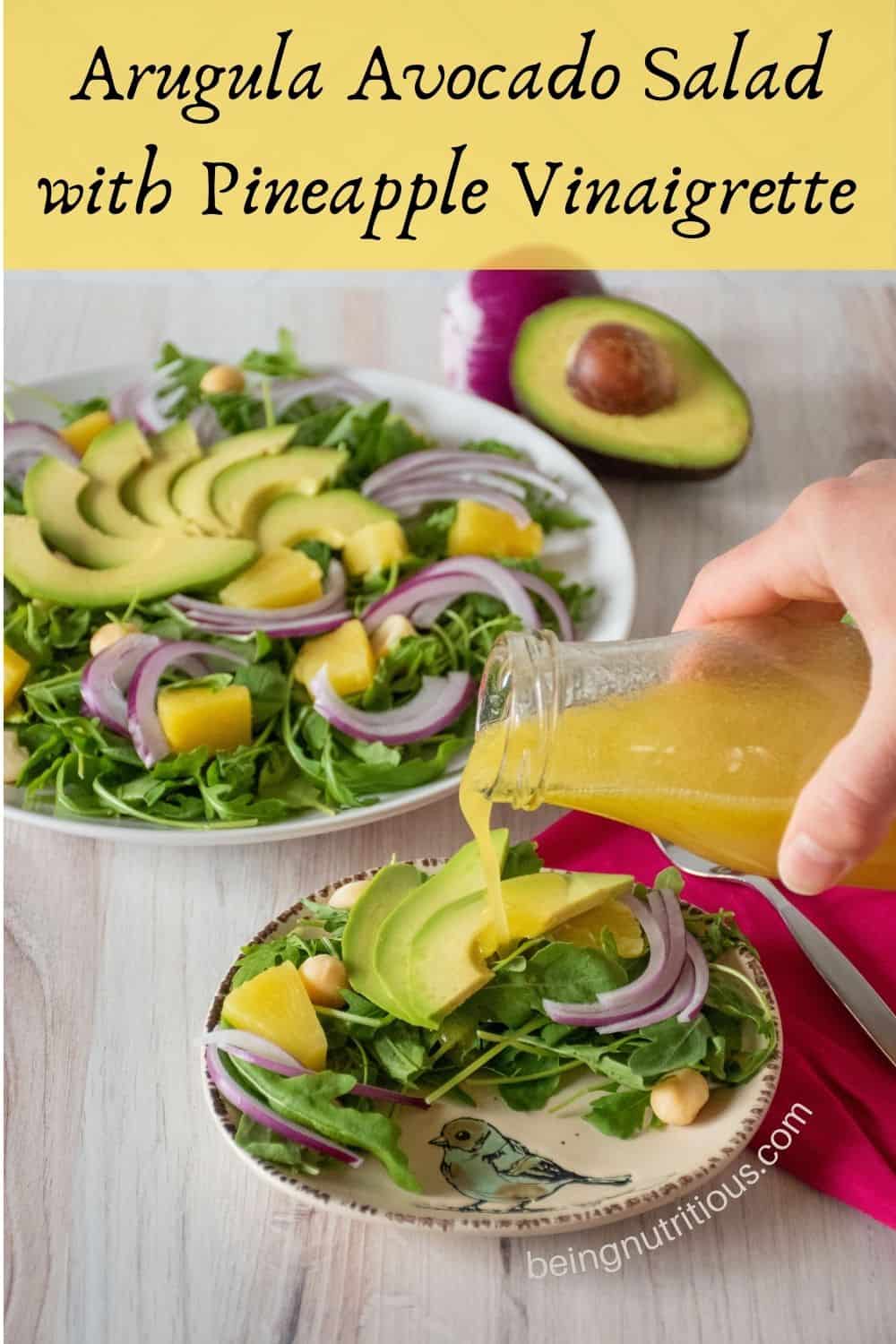 Salad on a small serving dish with dressing being poured on. Text overlay: Arugula Avocado Salad with Pineapple Vinaigrette