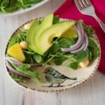 Salad with arugula, avocado, pineapple, red onion, and macadamia nuts on a small serving dish.