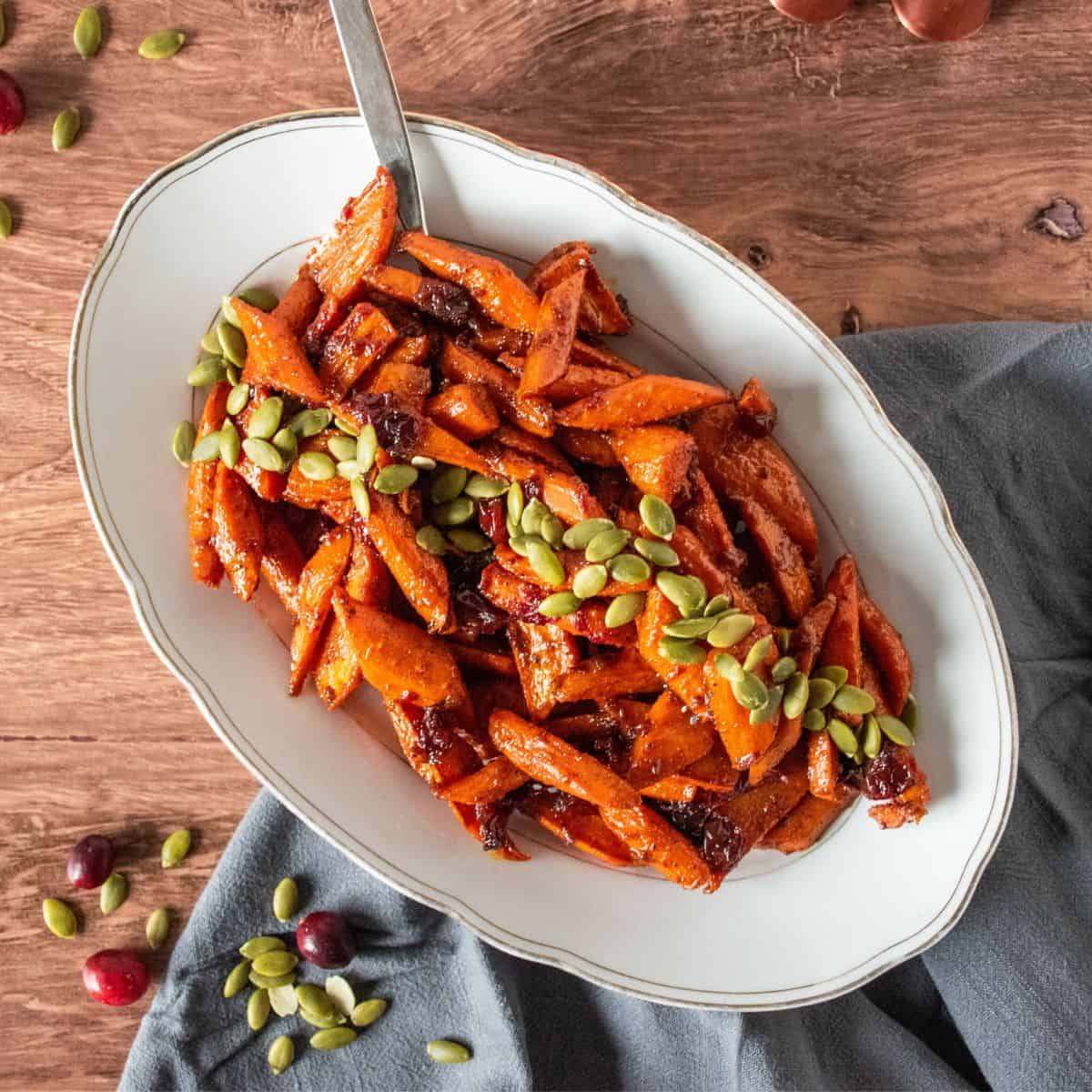Oval plate with glazed carrots on it, garnished with pepitas.