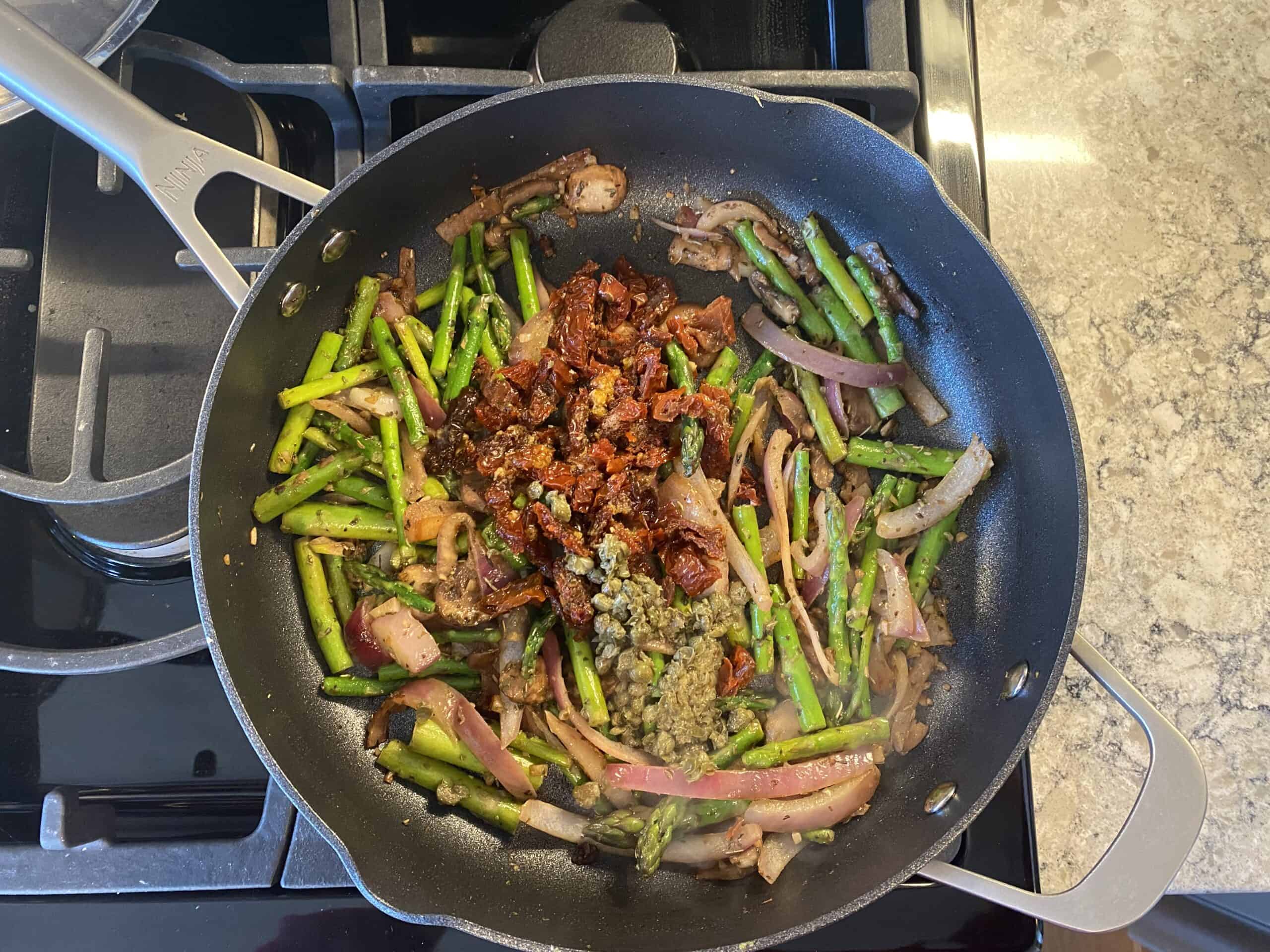 Sauteed vegetables in a pan, with sundried tomatoes and minced capers added.